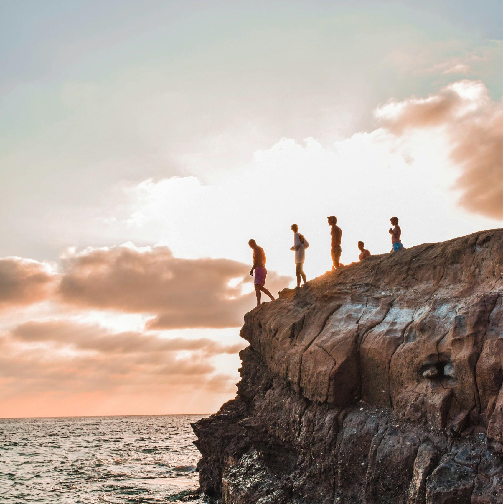 Group of people cliff jumping into the ocean at sunset. Captured in high detail.