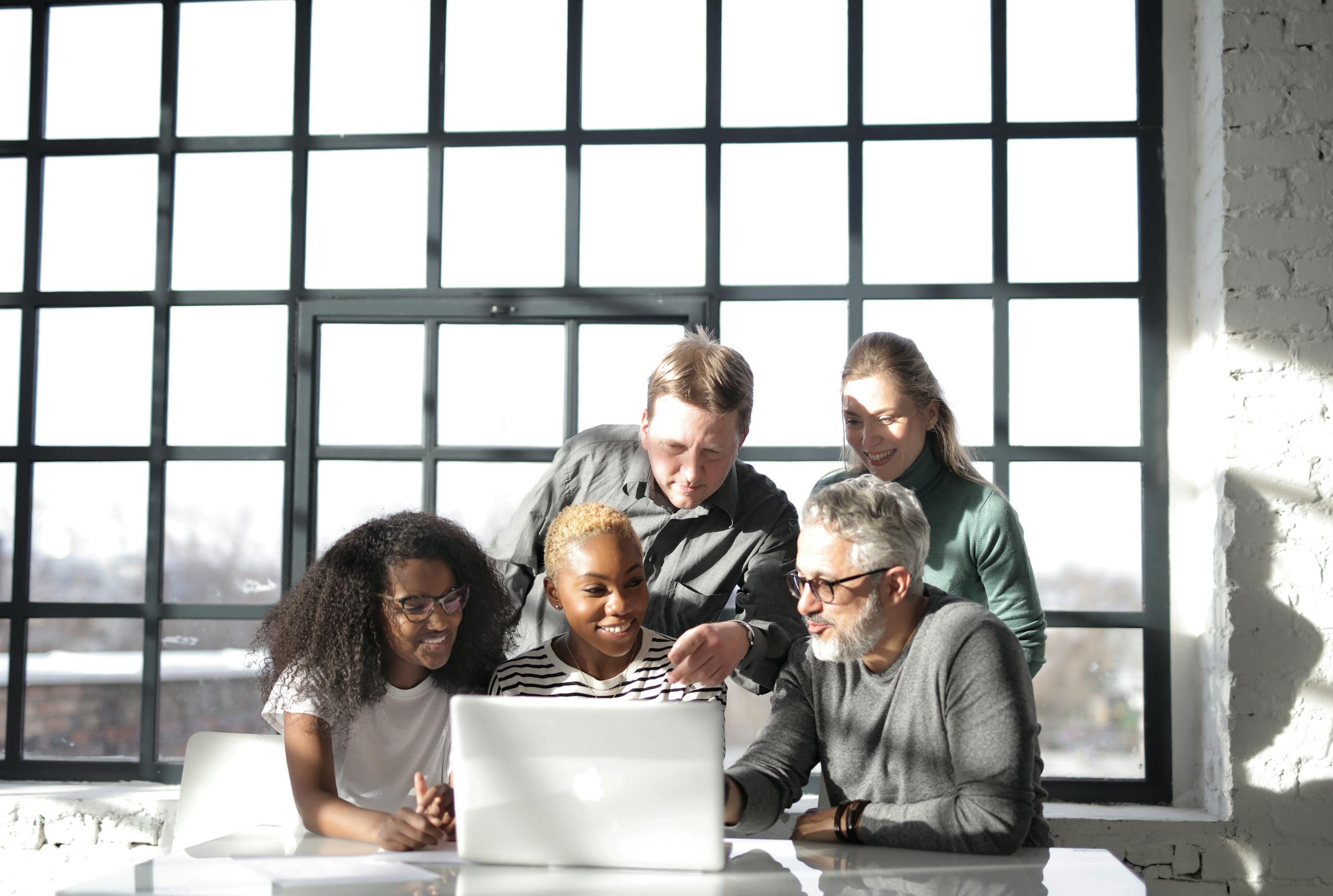 A diverse group of adults collaborating around a laptop in a bright, modern office.