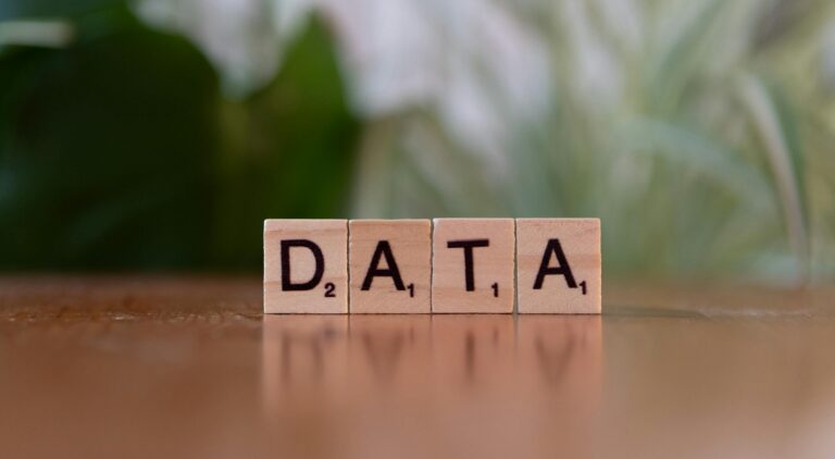 Scrabble tiles spelling 'DATA' on a wooden table with a blurred plant background.